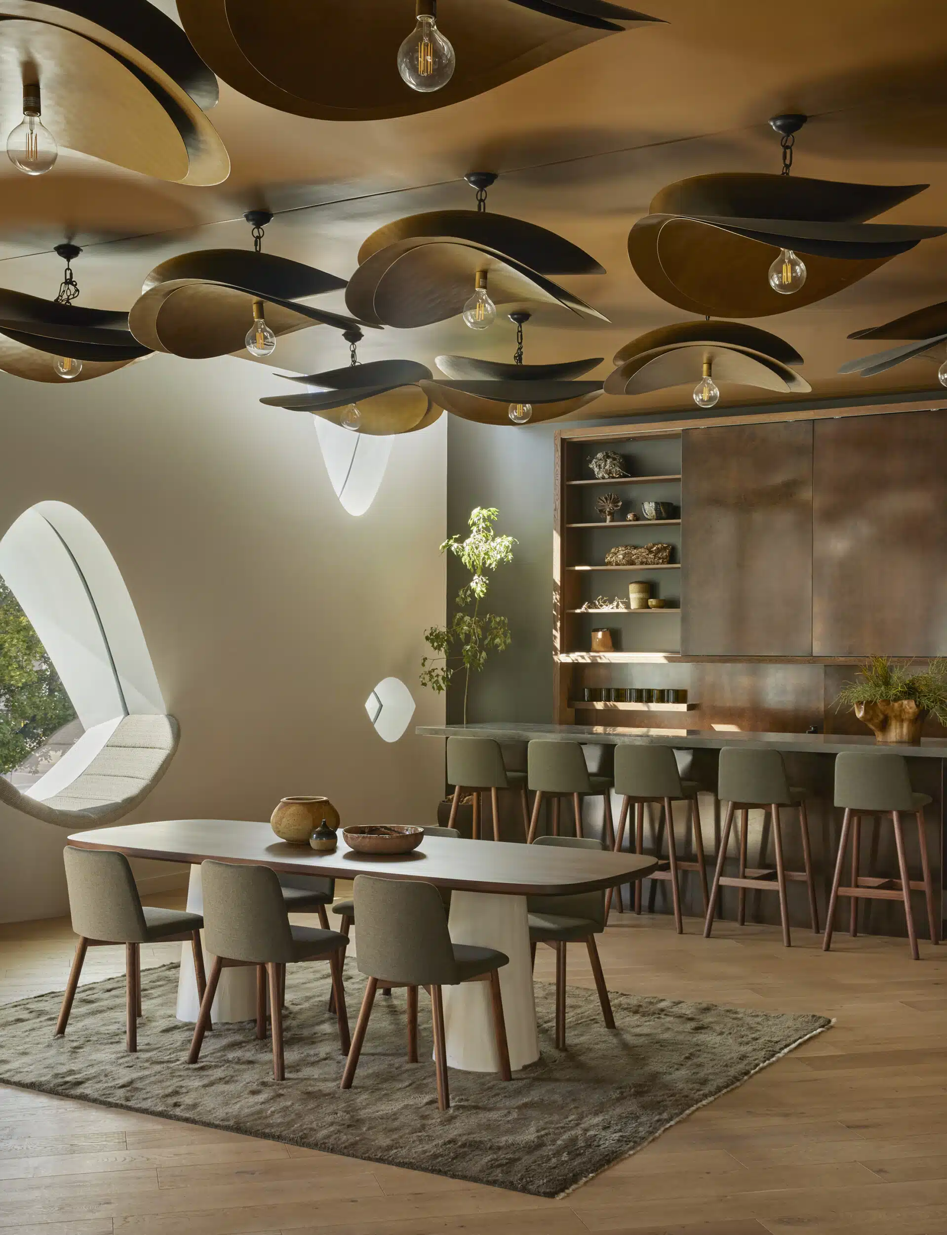 Level 02 meeting space with a long table, an oval window, and a ceiling of layered, leaf-like wooden discs above a bar.