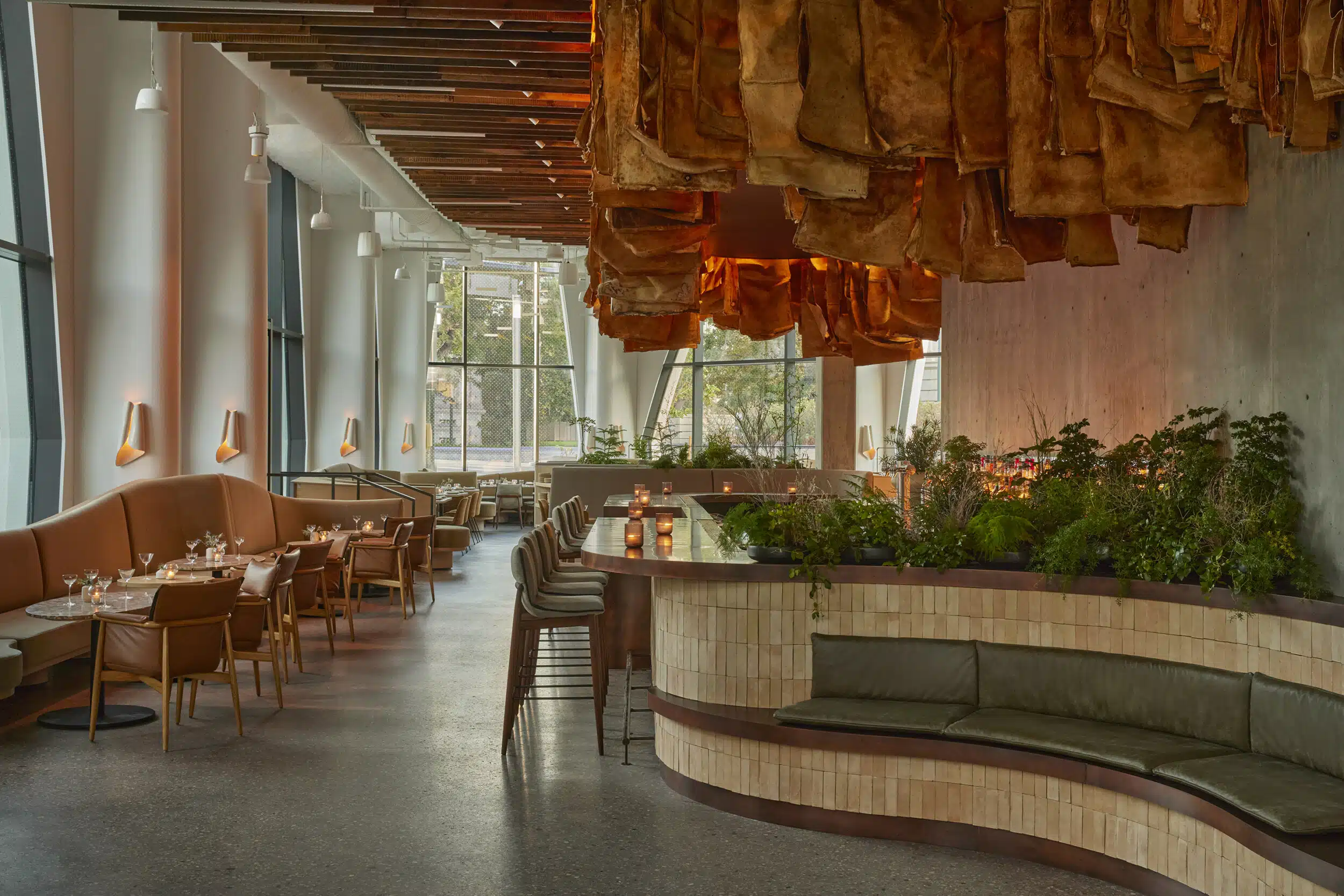 Pasque restaurant with curved banquette seating, a planter of greenery, and copper-toned sculptural light fixtures overhead.