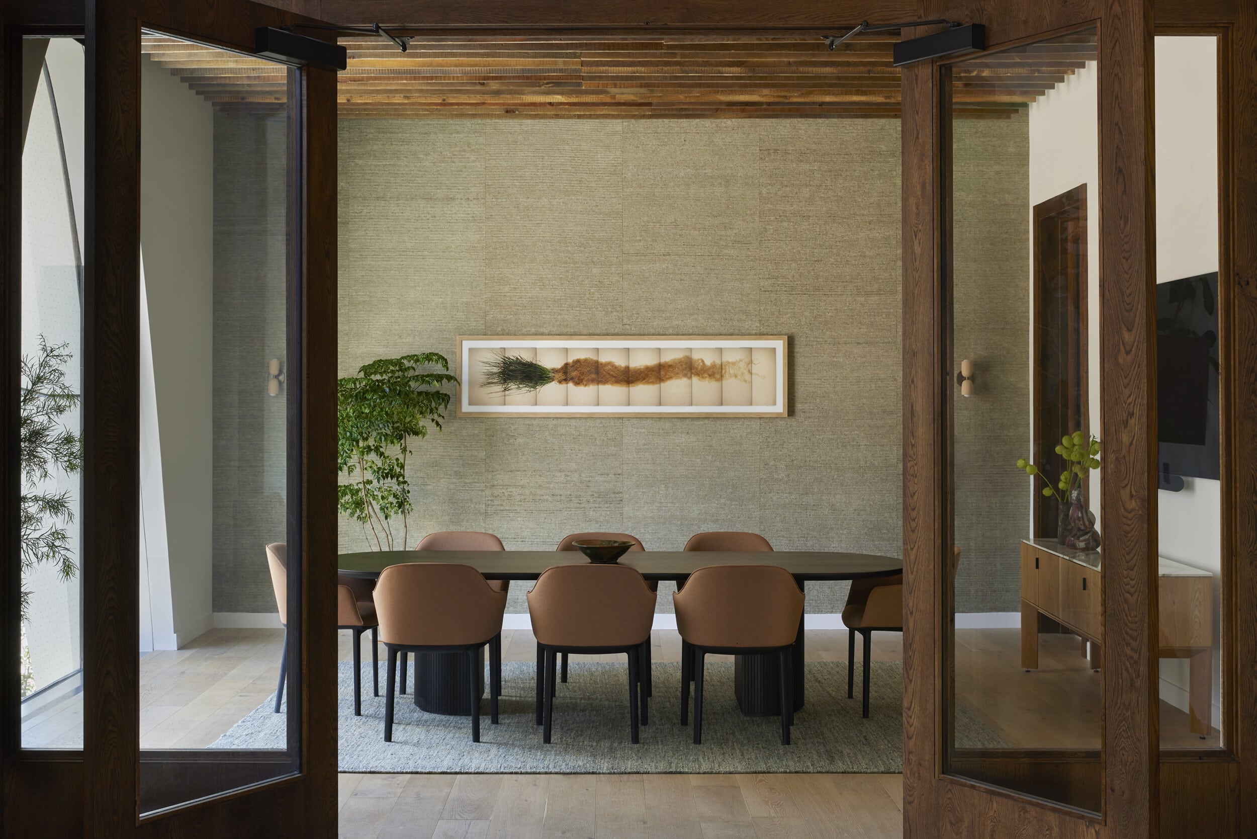 A view of the Enclave through wooden doors into a private meeting room with a long table, leather chairs, and a horizontal artwork on a gray wall.