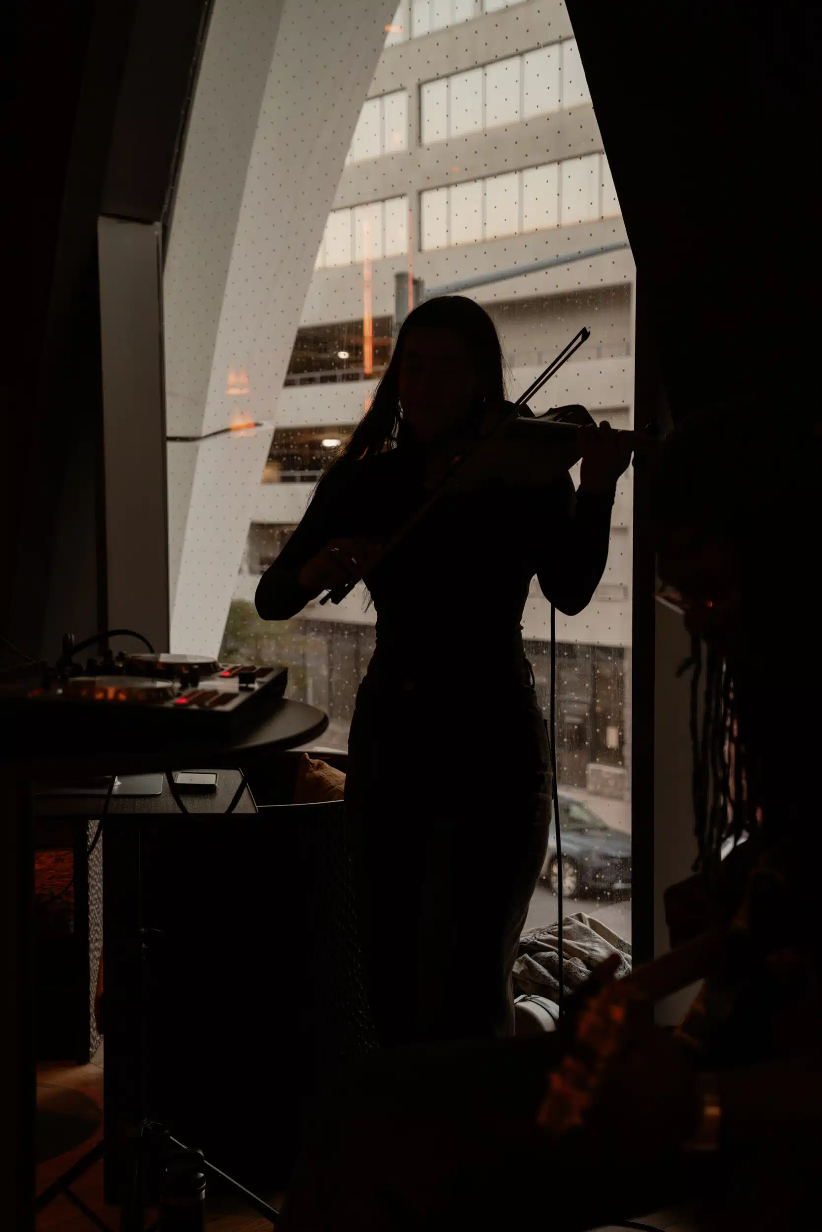 Violinist silhouetted against an arched window, playing beside a DJ controller.