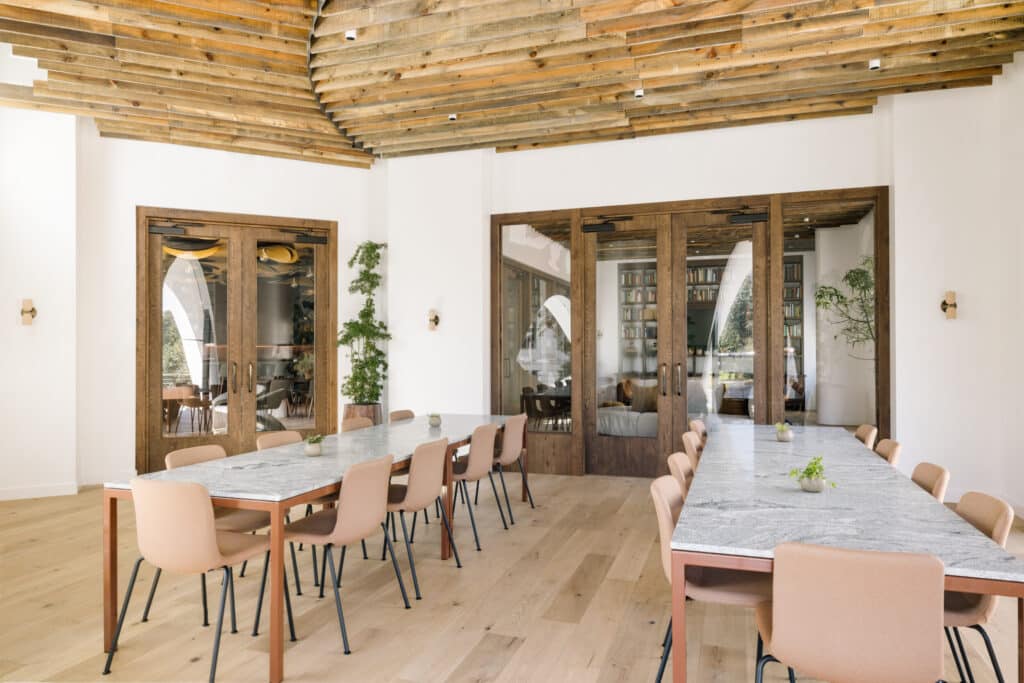 The Overlook meeting space with marble-topped tables, blush chairs, and a rustic wood ceiling, lined with wooden glass-paned doors.